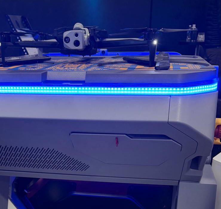 Quadcopter with a sensor gimbal sitting on top of a white automated docking station lit with a blue LED strip